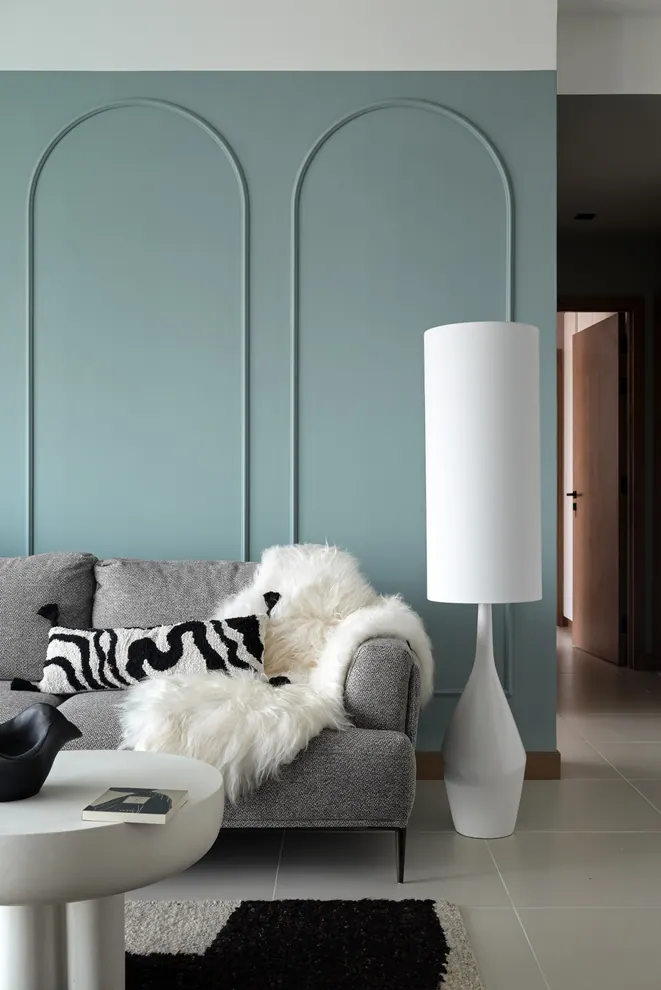 Teal wall with arched mouldings behind a grey tweed sofa with a sheepskin throw