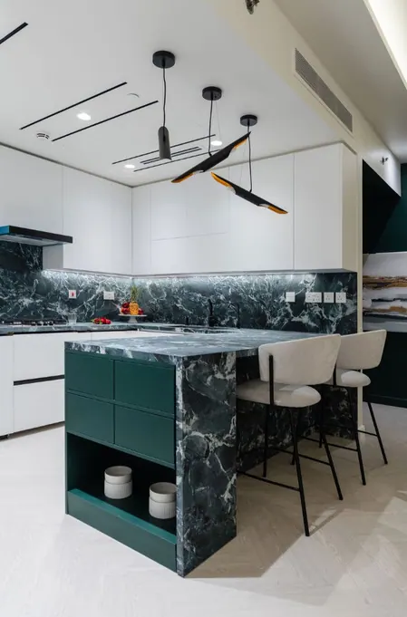 White kitchen with a green marble island, splashback and black pendants