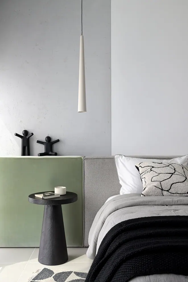 Bedside with a sage green panel, a black pedestal table and a cone pendant