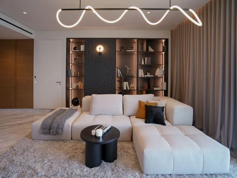 Living room with a white modular sofa, built-in black shelving and a looping LED pendant