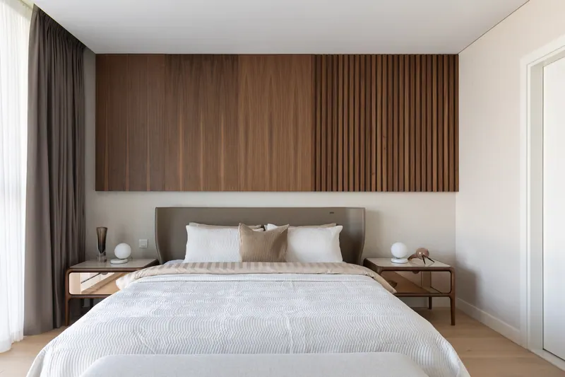 Guest bedroom with a walnut veneer and slat panel above a taupe leather bed