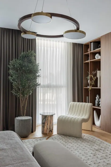 Bedroom lounge corner with a ribbed cream armchair, olive tree and walnut bookcase