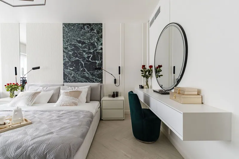 Bedroom with a floating dressing table, a round black-framed mirror and a green velvet chair
