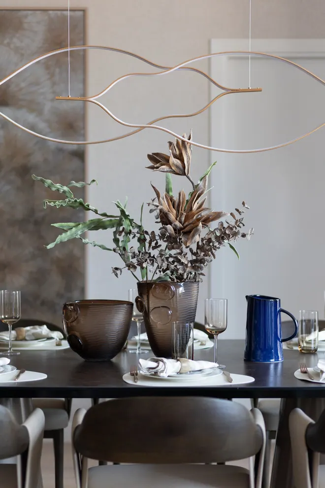 Dining table styled with dried flowers, brown glass vases and a blue jug under a brass line pendant