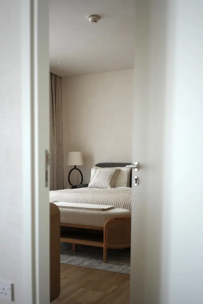 Bedroom seen through the door: striped bedding, a cane bench and a ceramic table lamp
