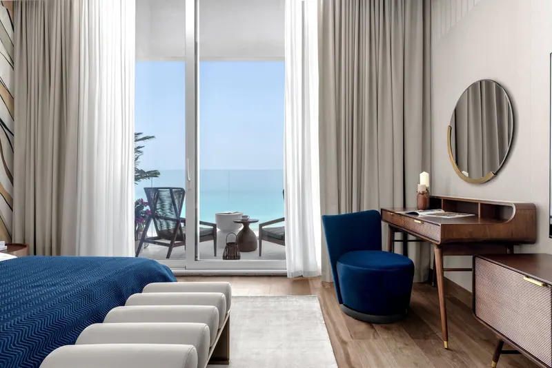 Bedroom opening onto a balcony with a sea view, blue bedspread and walnut dressing table
